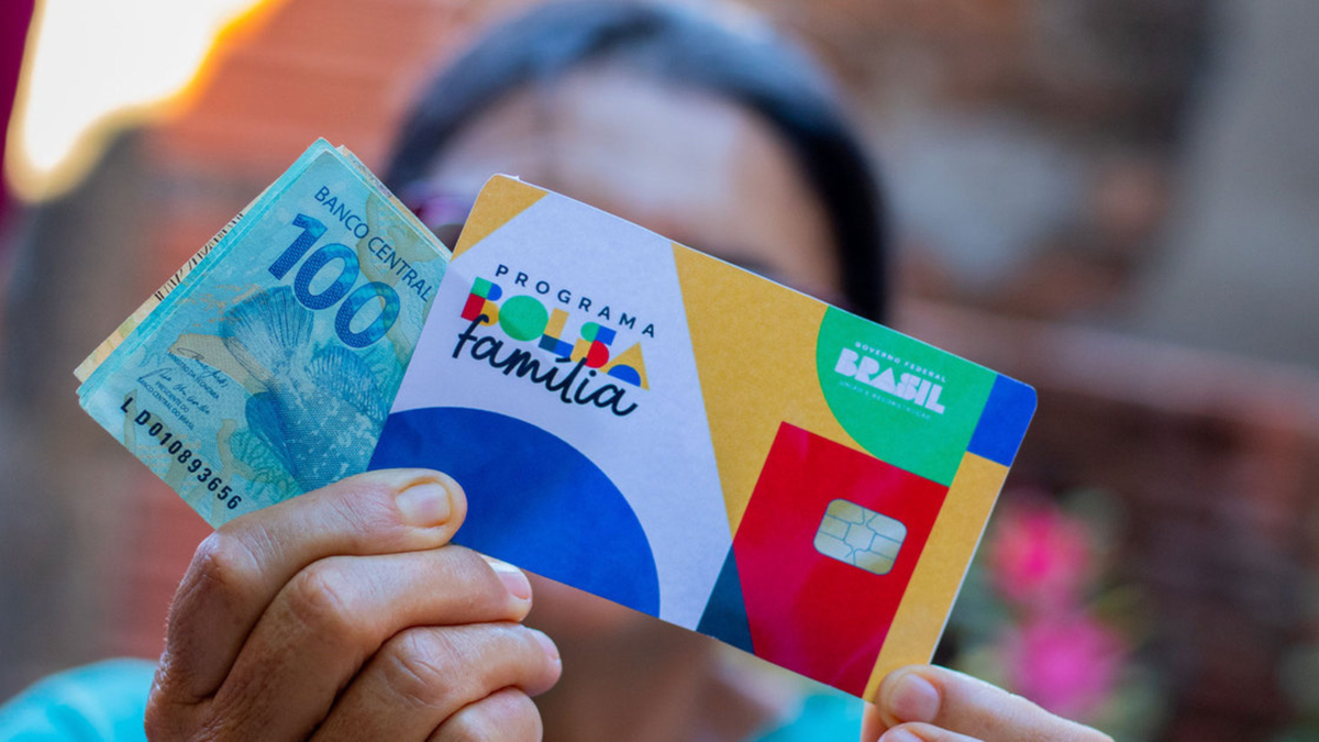 Pessoa segura cartão do Bolsa Família e notas de cem reais - divulgação/Agência Brasil